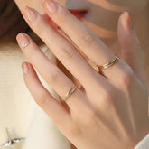 Model hand with two twisted gold rings—one plain, one diamond—covering lips