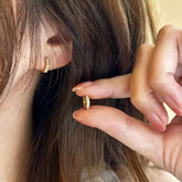 Woman wearing single hexagon pavé huggie earring, holding the matching hoop near ear