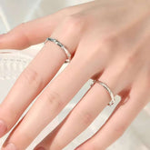 Hand wearing two slim bamboo-texture gold rings—plain and diamond pavé—against clear glass