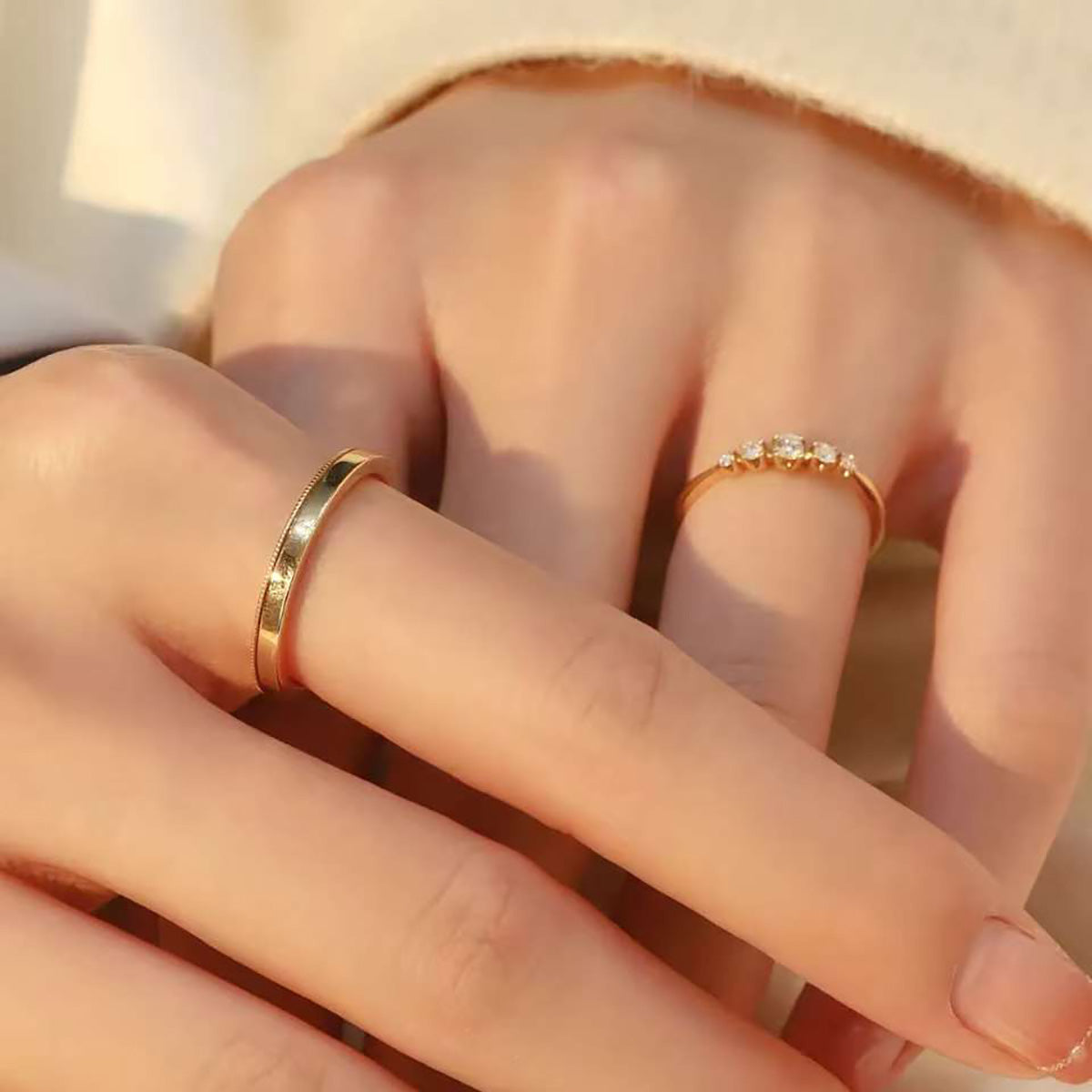 
Woman’s hand wearing 18K gold diamond ring set – elegant five-stone diamond band and polished plain ring