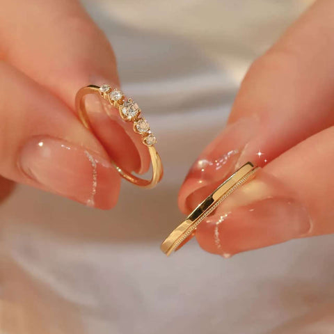 Hand holding two 18K gold rings – one diamond band with five lab-grown diamonds, one classic plain band

