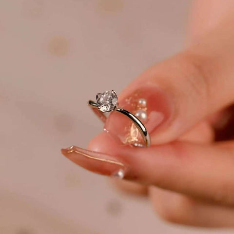 Delicate solitaire ring in a sculptural four-prong setting, held lightly between fingertips