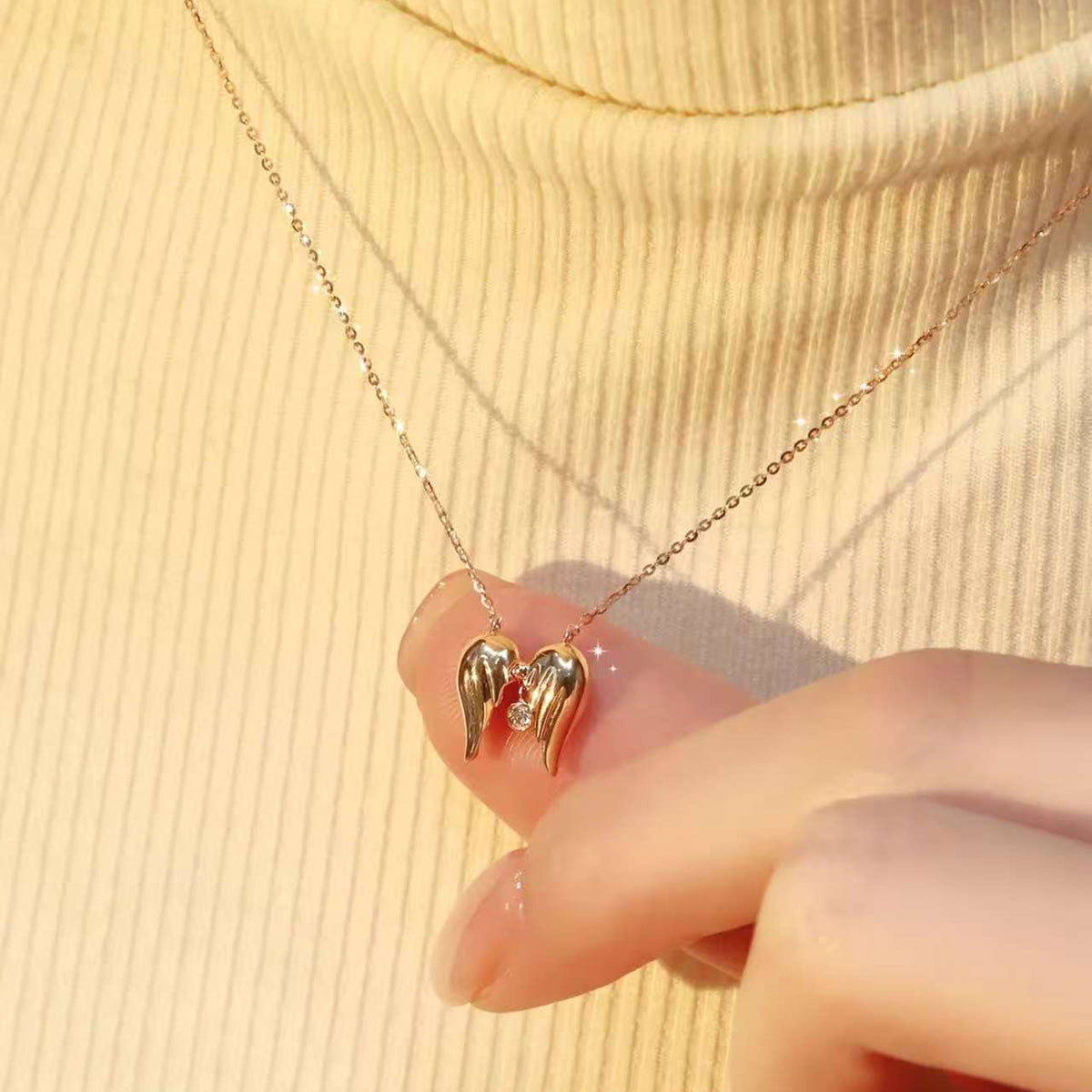 Fingers holding an angel-wings diamond necklace, pendant floating in light