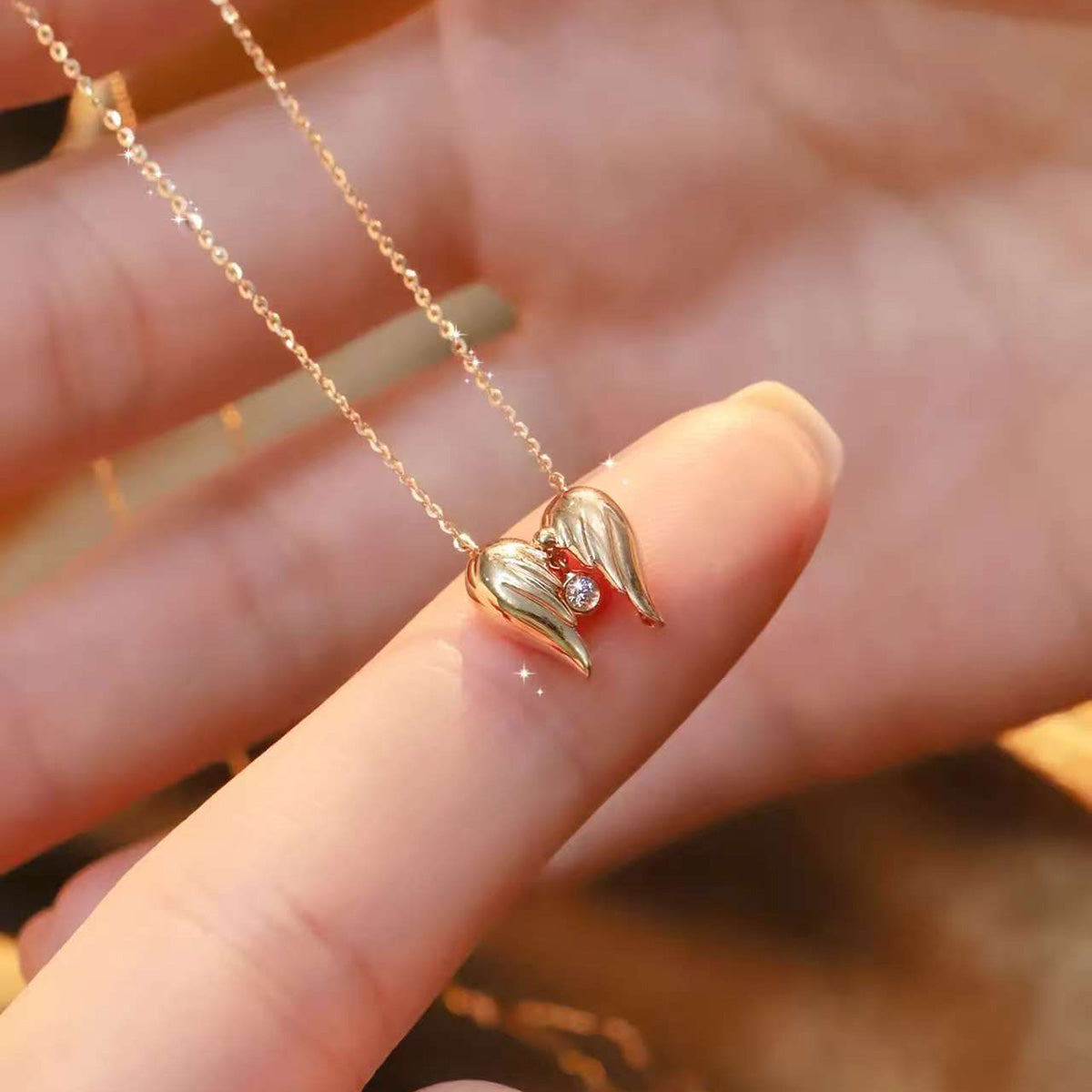Warm back-lit scene of heart-shaped wing pendant on delicate gold chain