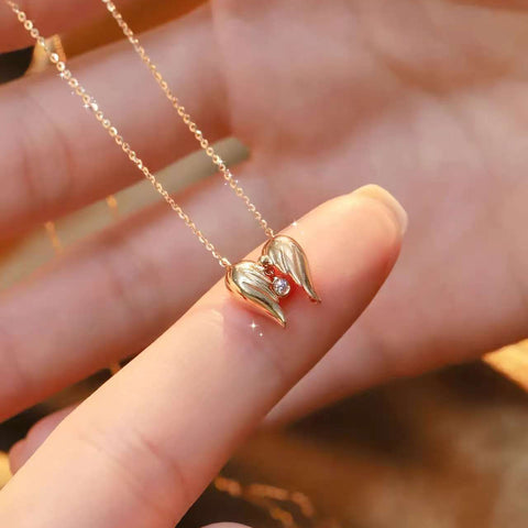 Warm back-lit scene of heart-shaped wing pendant on delicate gold chain