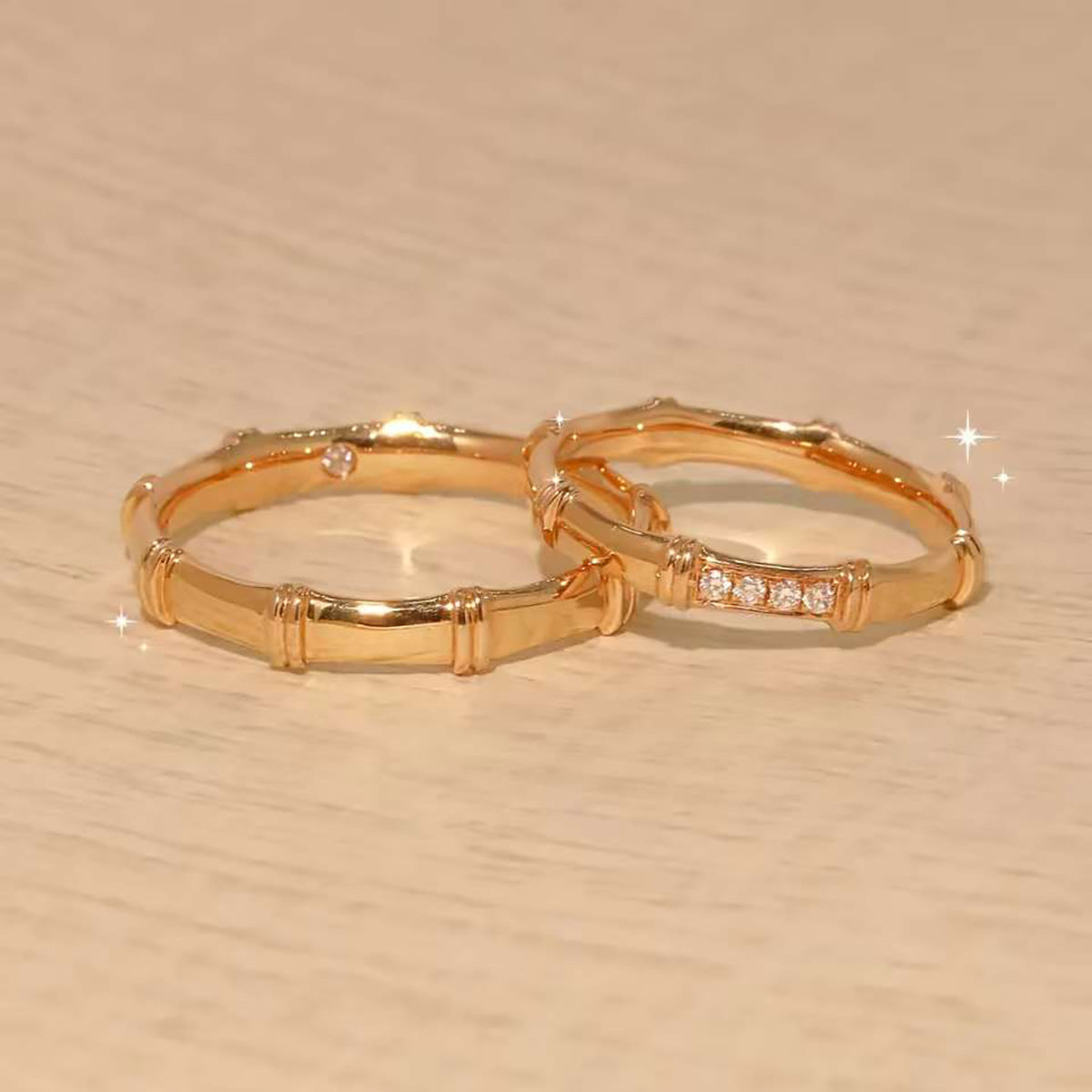 Pair of bamboo-texture gold rings—one with diamonds—sparkling on wooden surface