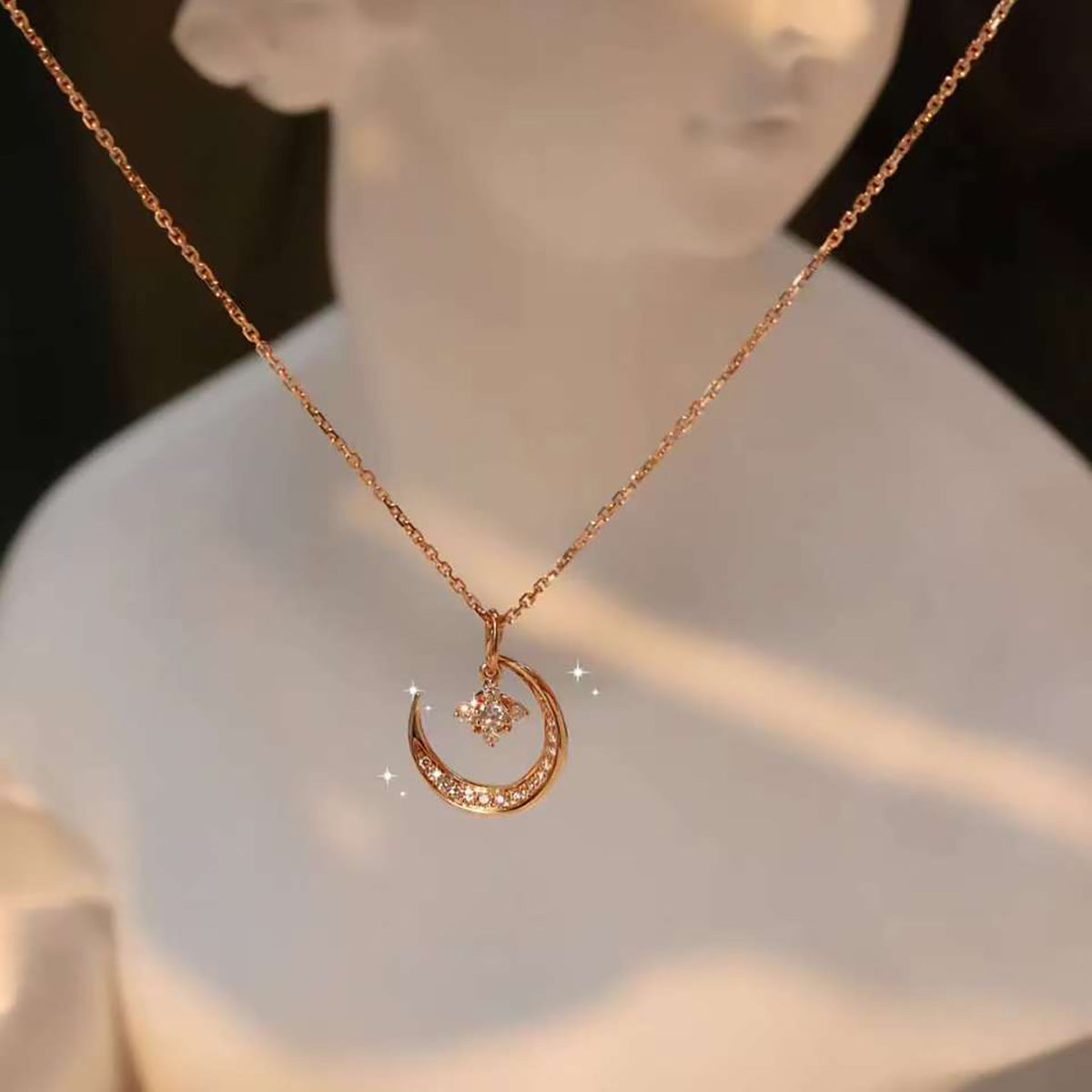 Crescent-moon diamond pendant displayed on a white bust under warm light