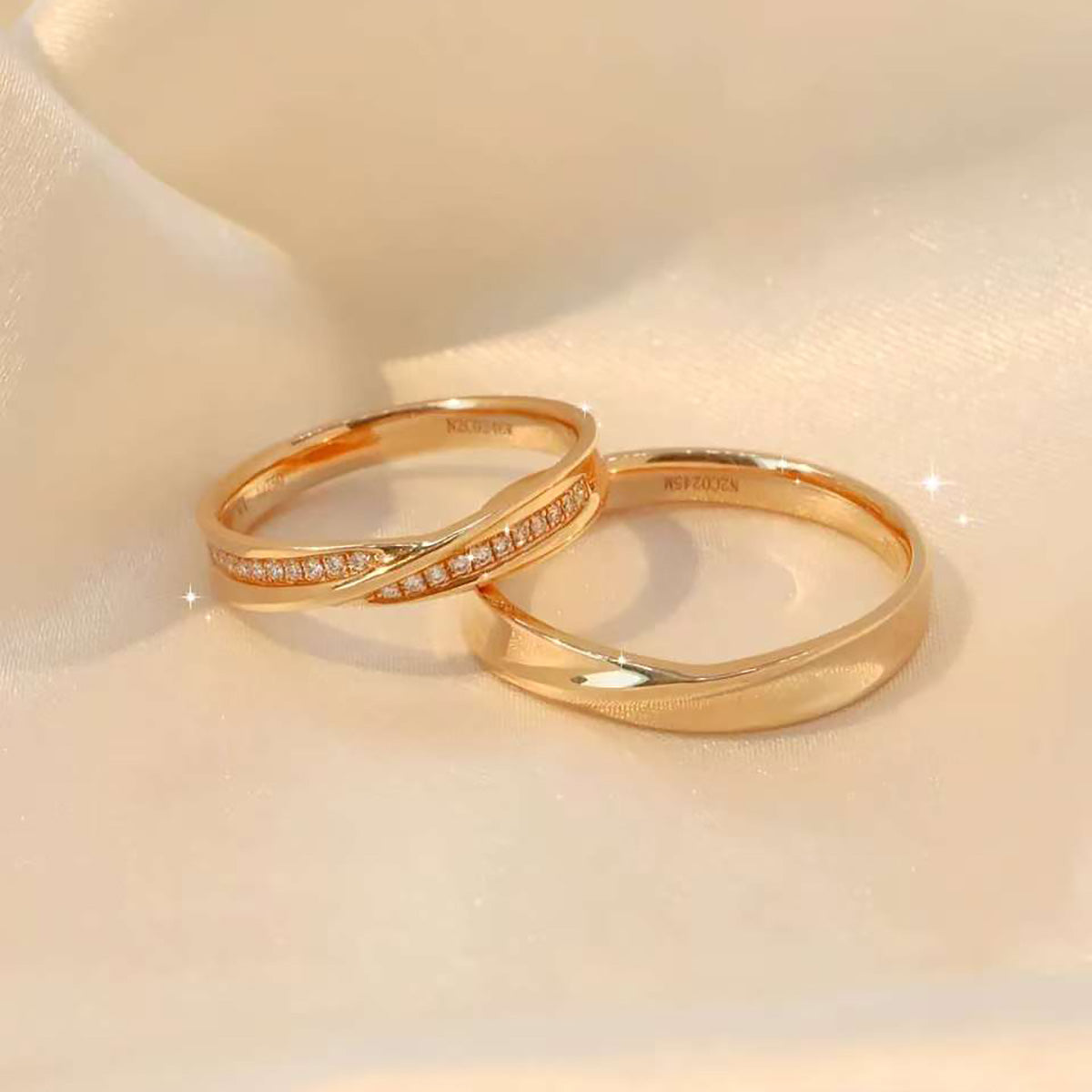 Pair of crossover yellow-gold rings (diamond + plain) sparkling on satin fabric