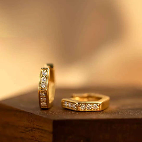 Close-up of pair of hexagon pavé mini hoops on wood block, warm light