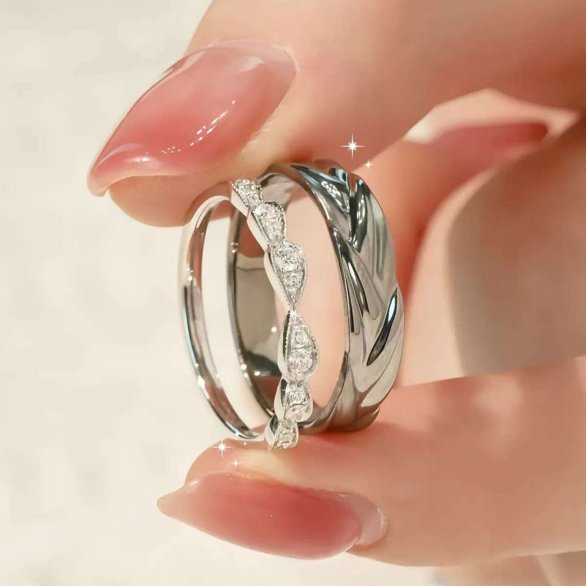woman holding two matching sterling silver couple rings with twisted leaf pavé design and classic men’s band
