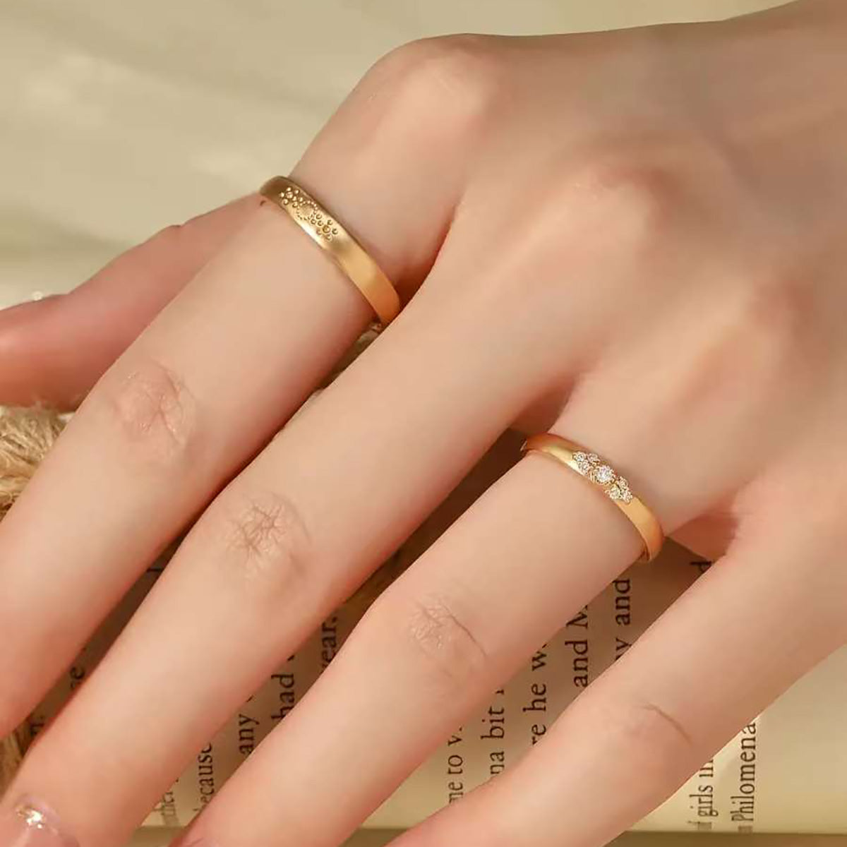 Hand wearing matte sunburst gold ring and trio-diamond gold ring on adjacent fingers